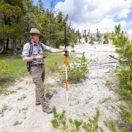 lt= a person wearing a park ranger uniform and hat carrying a GPS pole and device