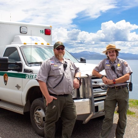 two people in park ranger uniforms standing in front of a medical ambulance vehicle