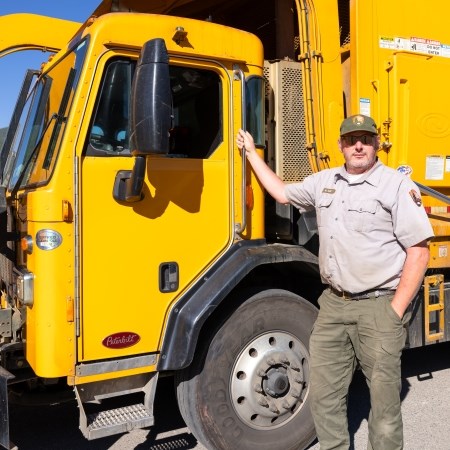a park ranger standing next to a large yellow construction vehicle
