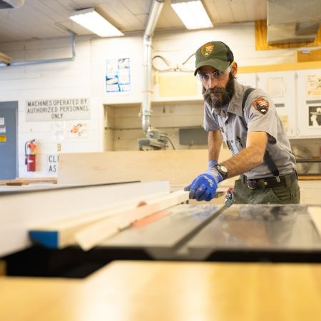 a park ranger using a machine to cut a long piece of wood