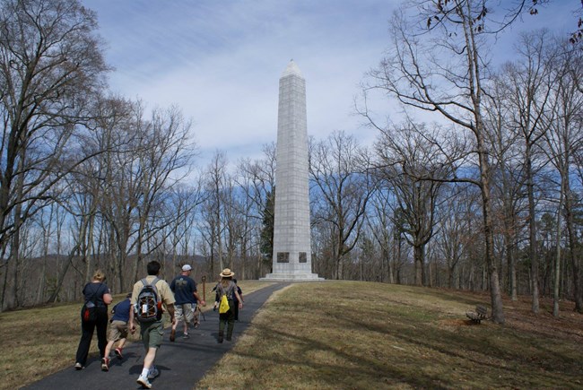 Visitors walk toward Centennial Monument. Group of visitors walk paved path to monument.