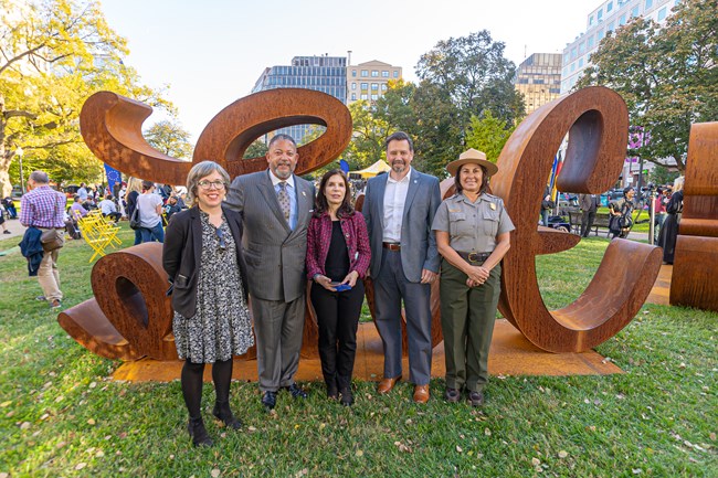 Members of the Golden Triangle BID pose with NAMA Superintendent Jeff Reinbold and ranger Catherine Cilfone in front of the Love Hate art installation at Farragut Square, November 9, 2021