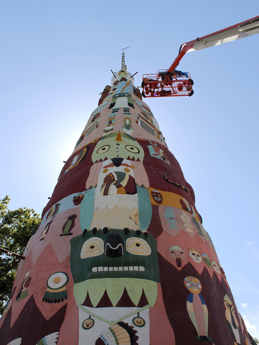 Looking up a tall multicolored pole with various images and a lift basket near the top.