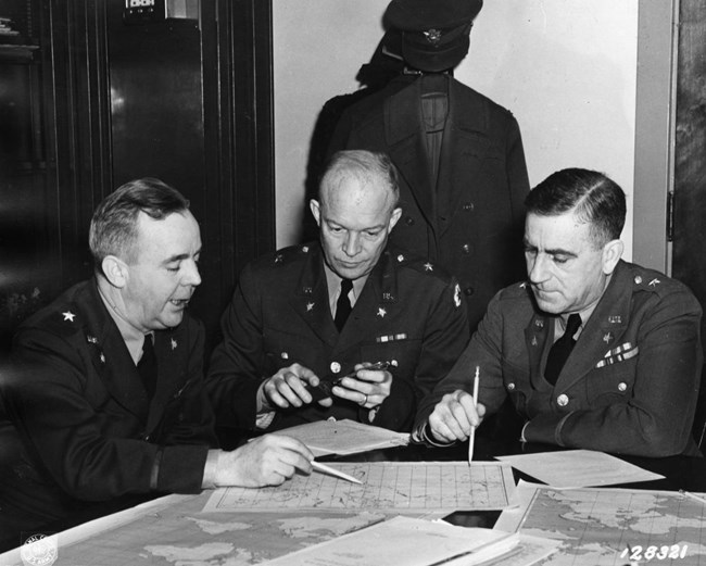 Three men in military uniforms are seated at a table working