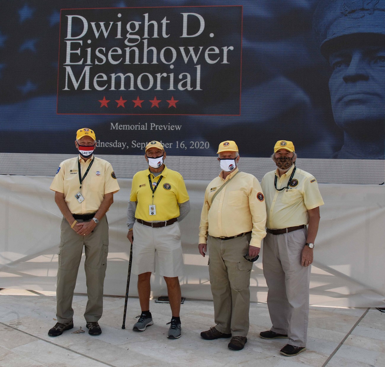 Four men in yellow pose by statues.