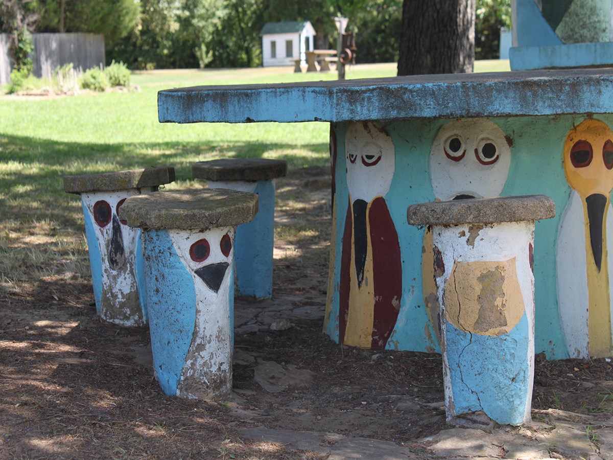 Cement picnic table and cement stools with weathered painted bird caricatures on the bases.