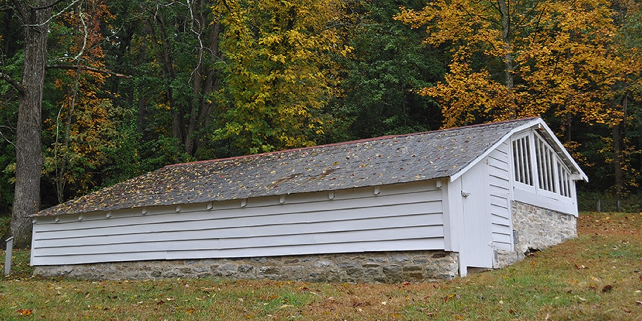 A long building is built on a rock foundation with one side all wood and the opposite side in window panes. A small door allows access on each end.