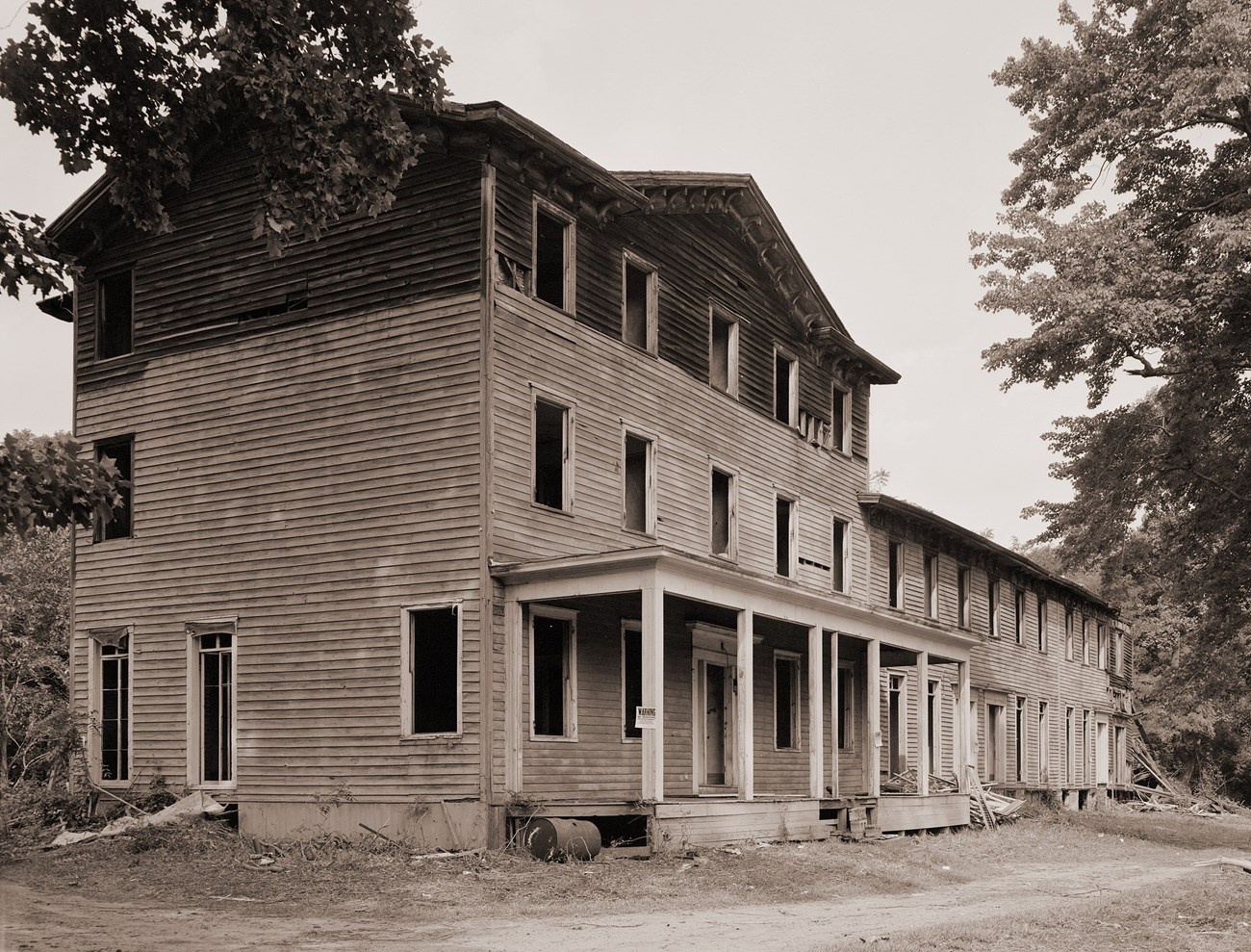 Three story building with wooden siding and all windows broken and without glass and a two story extension attatched to the right side