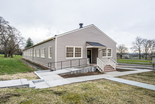 728 exterior and sidewalk improvements A one-story, historic grey building with cream trim is shown, along with nearby sidewalks and accessibility ramp, as well as small grassy areas.