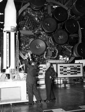 A black and white image showing two men standing next to a model rocket