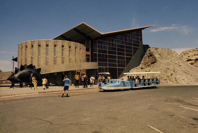 Dinosaur Quarry Visitor Center A photo taken from the parking lot shows a building with a tall, glass window walls, an angular roof, and an attached cyclorama
