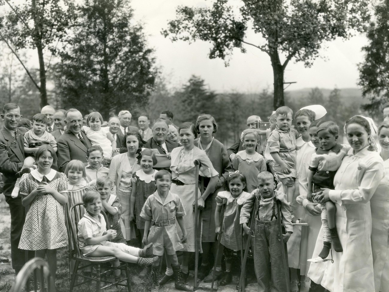 FDR surrounded by a group of children and adults, some supporting themselves with crutches.