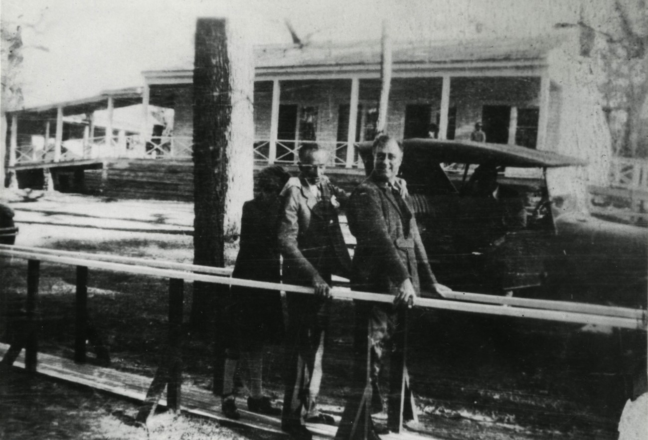 FDR with two people behind practing walking with parallel bars.