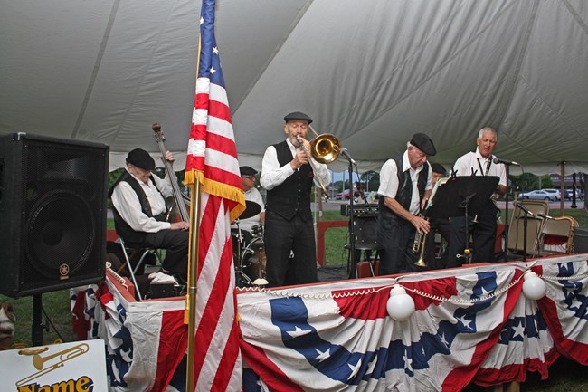 A crowd of people dancing under a tent with a "big band" playing them music.