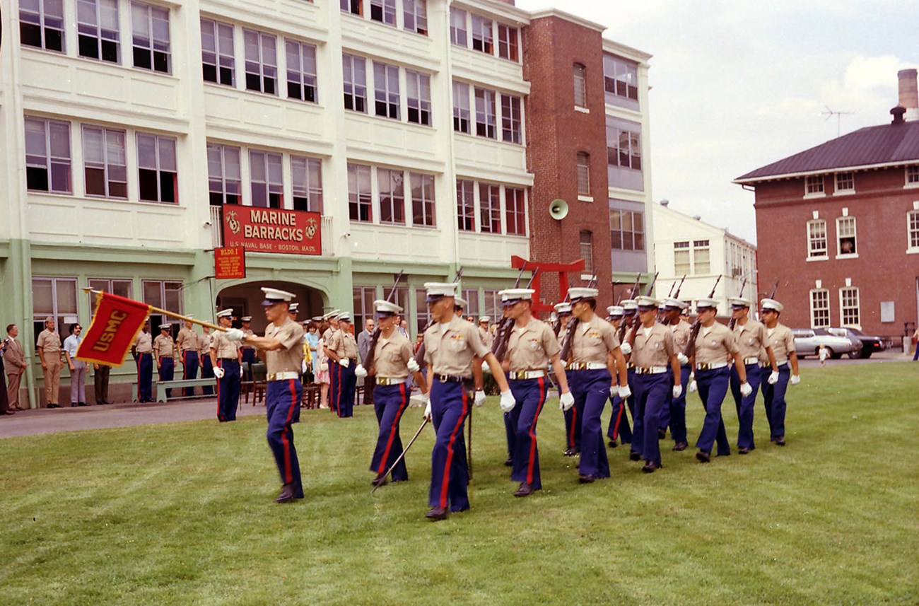Marines in dress uniform marching on the parade ground in front of the Marine Barracks.