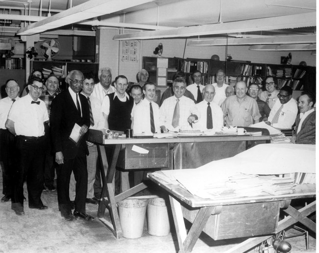 A group of men in a work space posing for a picture. Allan Crite is to the left.