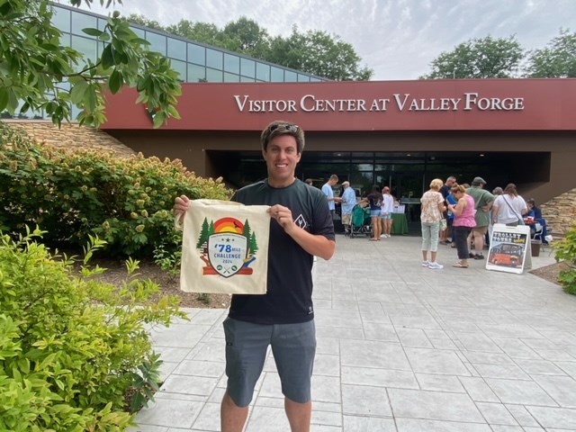 78 Mile Challenge 250 level 2024 A smiling man standing in front of the Valley Forge visitor center holds up a tote bag with the 2024 logo on it