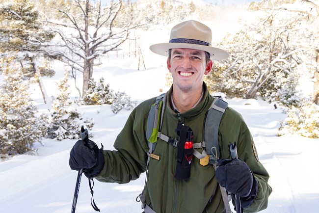 A park ranger on skis carries bear spray on his backpack.