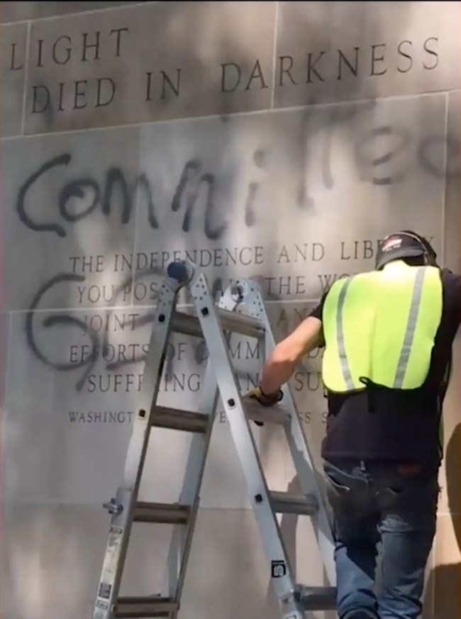 Next to the graffiti, a conservator in a yellow vest steps down a ladder.
