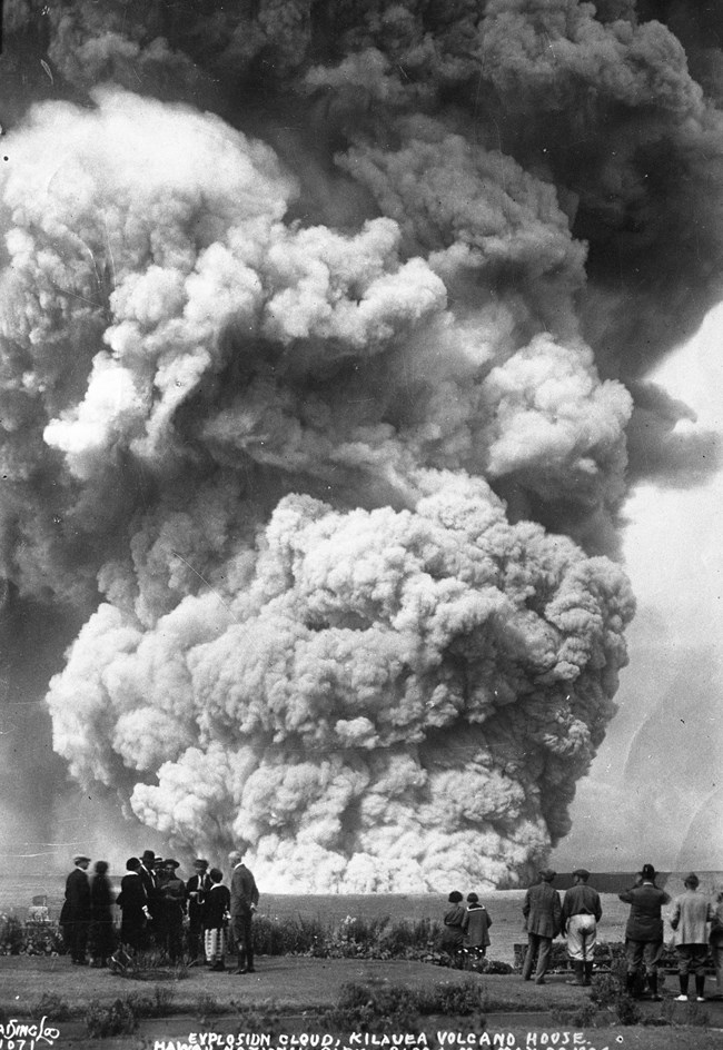 historic black and white photo of groups of people watchin a large steam cloud erupt from a volcano