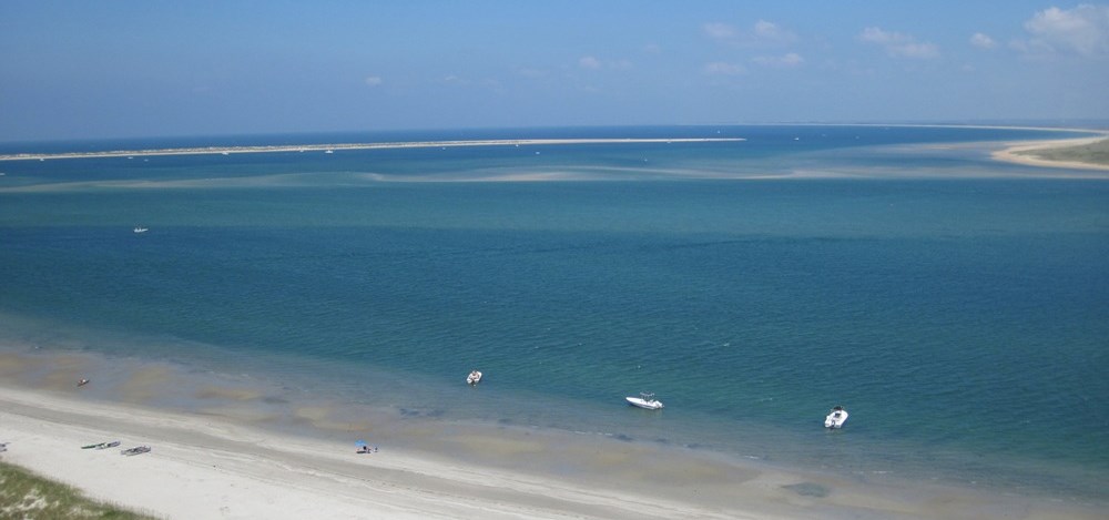 Shoals at the Hook of the Cape, Cape Lookout National Seashore. Aerial photo of a shoreline and blue ocean with three boats near shore.