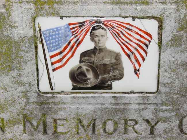 Cameo image from Elmwood Cemetery in Nashville, Tennessee, a fired ceramic that is set in the marble grave marker. Cameo image of a soldier with an American flag flying over him.