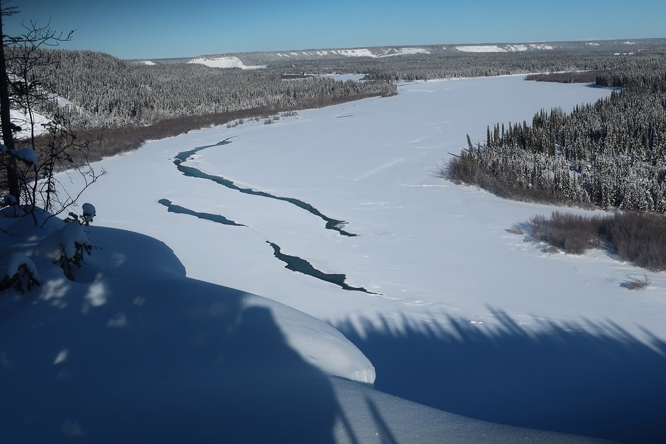 A snow-covered river in winter, with a little water showing.