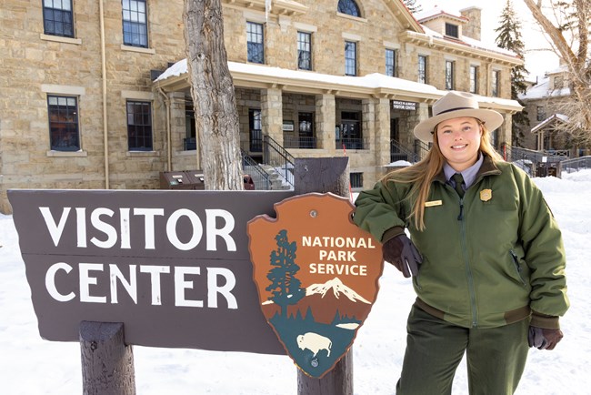 A park ranger stands by the sign in front of a visitor center.