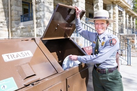 Stash Your Trash a park ranger throwing trash into a trash can