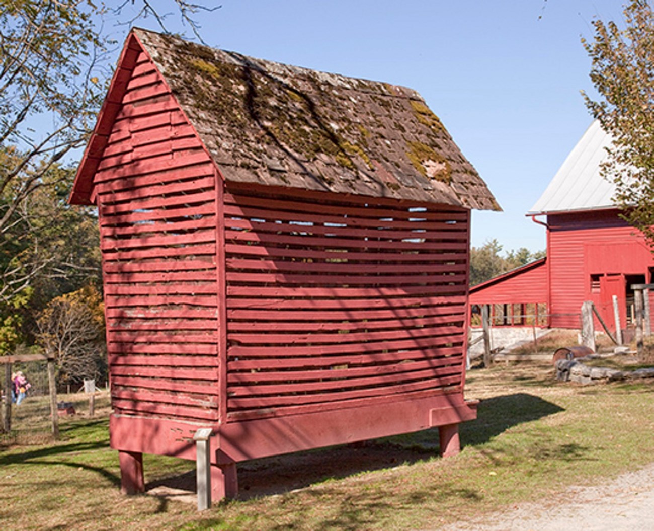 9 corn crib image A barn red shed with open wood slats and wire mesh allows air flow.