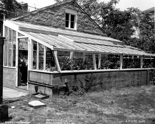 Greenhouse with a slanted glass roof next to a carriage house.