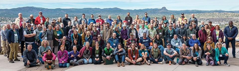 More than 100 people pose for a photo, mountains in distance.