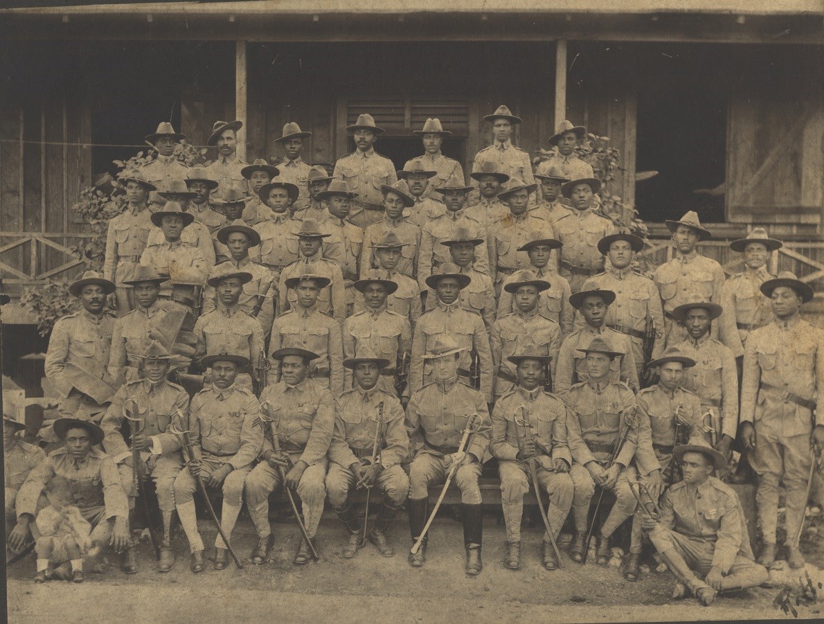 Black and white photo of company of African American soldiers standing in four rows shoulder to shoulder