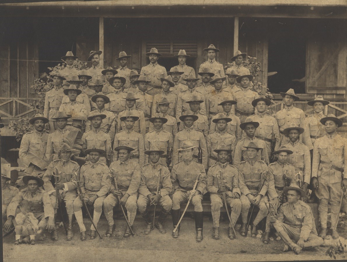 Charles Young (seated, 5th from left, front row) with his 9th Cavalry troopers while in the Philippines, c. 1902. Black and white photo of company of African American soldiers standing in four rows shoulder to shoulder