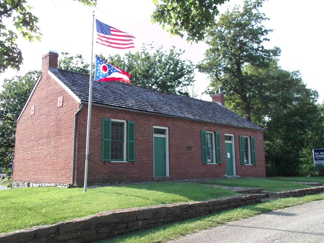 Photograph of a small, one-story brick building with a flag pole in front.