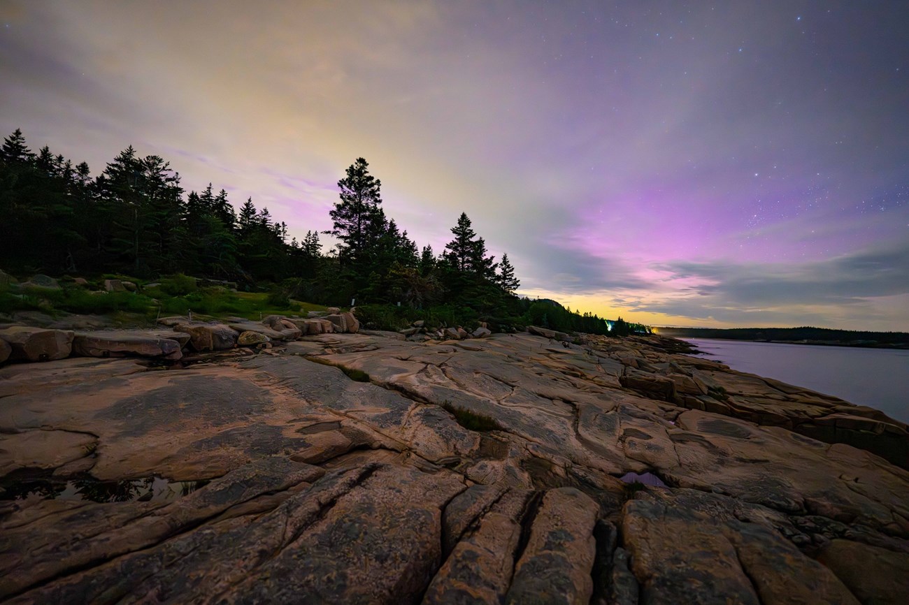Northern Lights at Acadia the night sky lights up with purples of the aurora over a rocky coastline