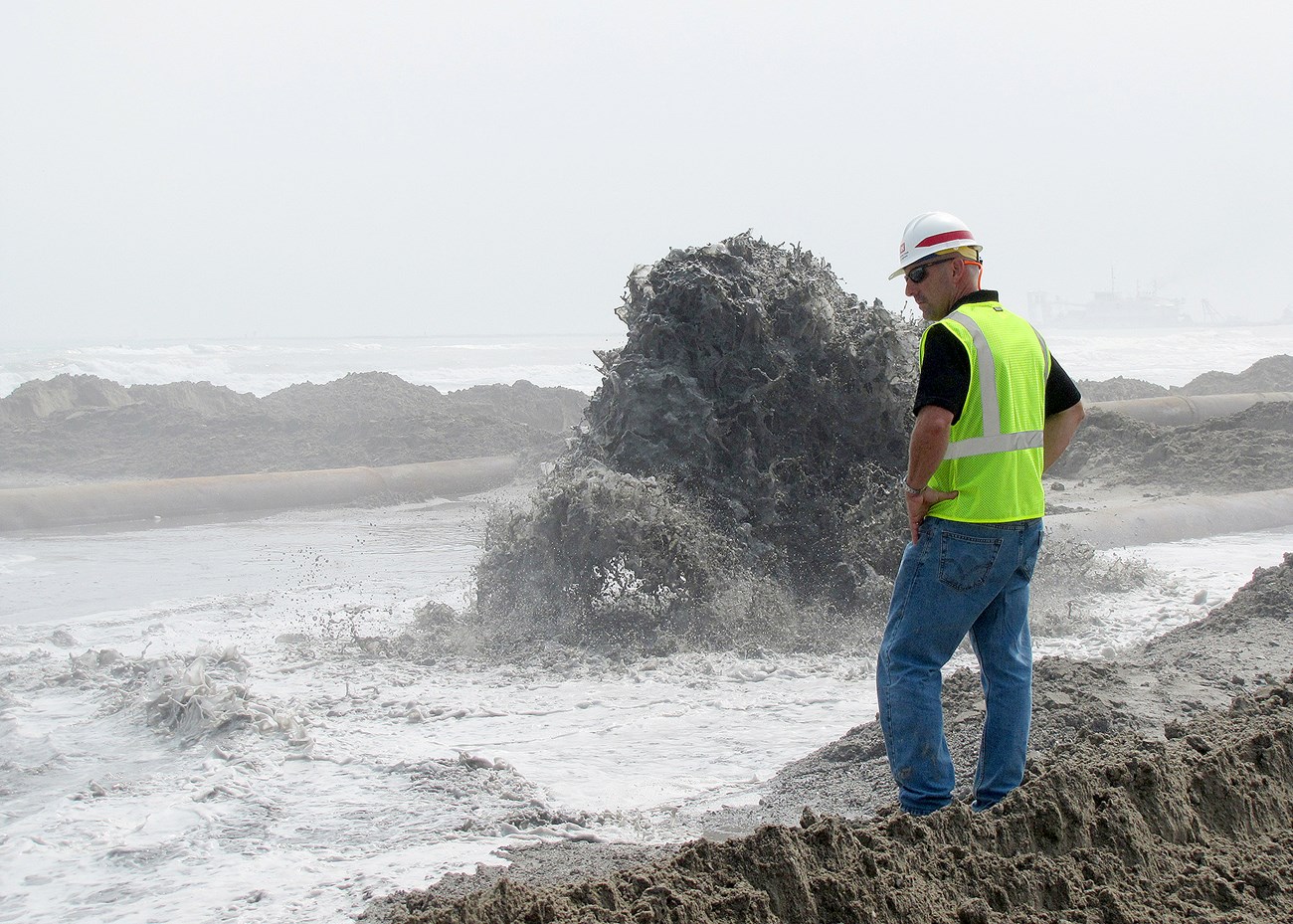 Army Corps of Engineers employee with safety vest and hard hat monitors placement of dredged material on South Padre Island
