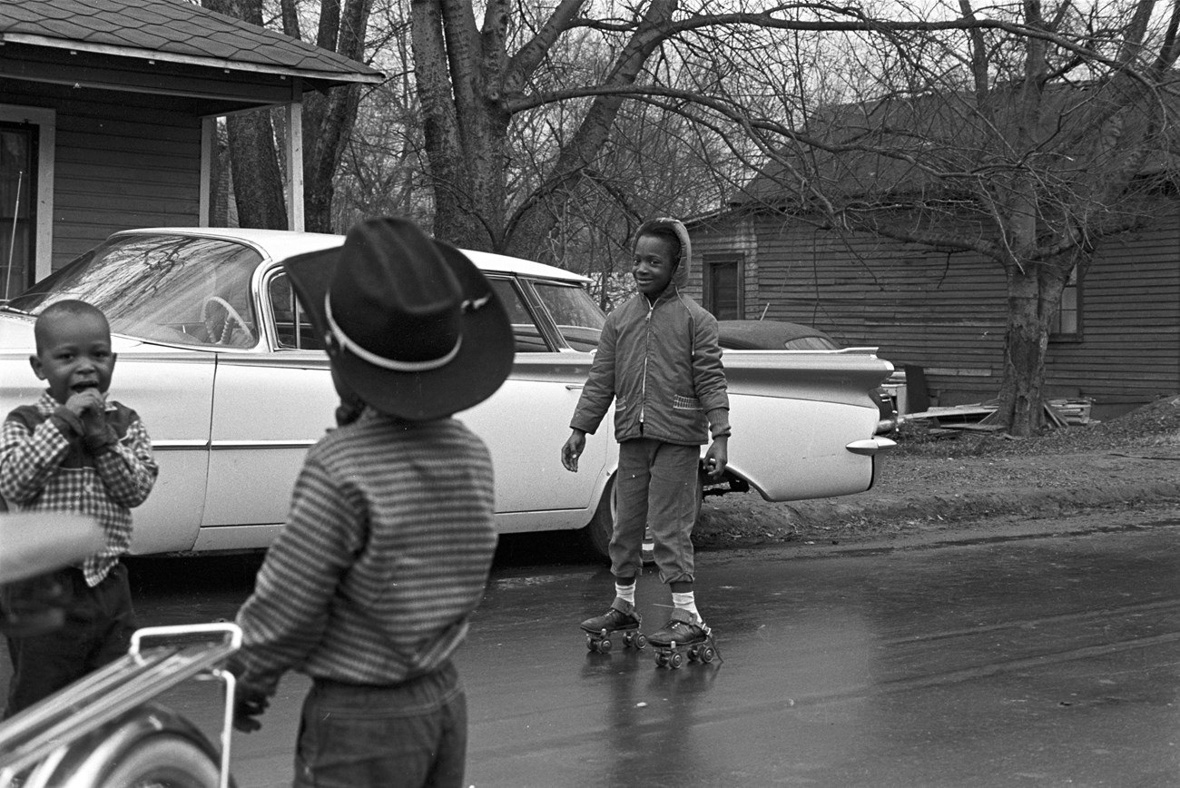 Girl skating in the street of a neighborhood in Montgomery, Alabama. Two other children are present.