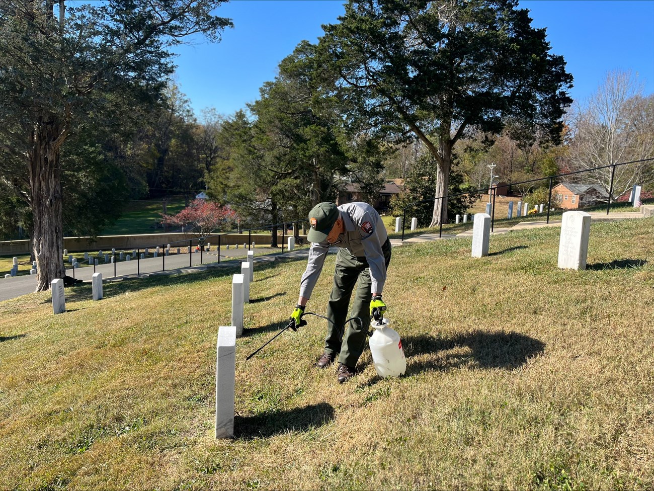 AJ conducts headstone cleaning operations in section W of Andrew Johnson National Historic Site Cemetery. Maintenance worker working on headstones in a cemetary on a sunny day using a cleaning applicator to clean historic headstones in the area.