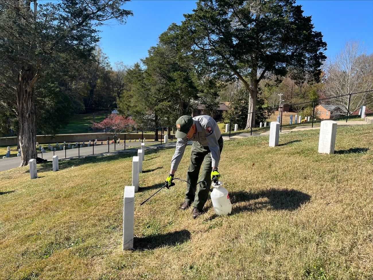 AJ conducts headstone cleaning operations in section W of Andrew Johnson National Historic Site Cemetery. Maintenance worker working on headstones in a cemetary on a sunny day using a cleaning applicator to clean historic headstones in the area.