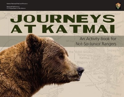 An image of the booklet cover. A profile picture of a Brown bear in the foreground and a grey-tone image of a map of Katmai in the background. Across the top is the title “Journeys at Katmai: An Activity Book for Not-So-Junior Rangers.