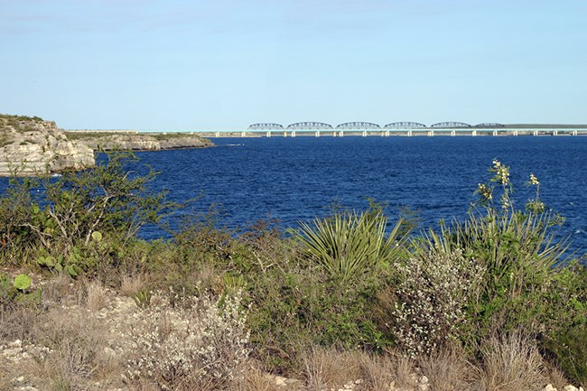 Amistad Reservoir Areservoir with desert plants on the bank and a bridge in the distance
