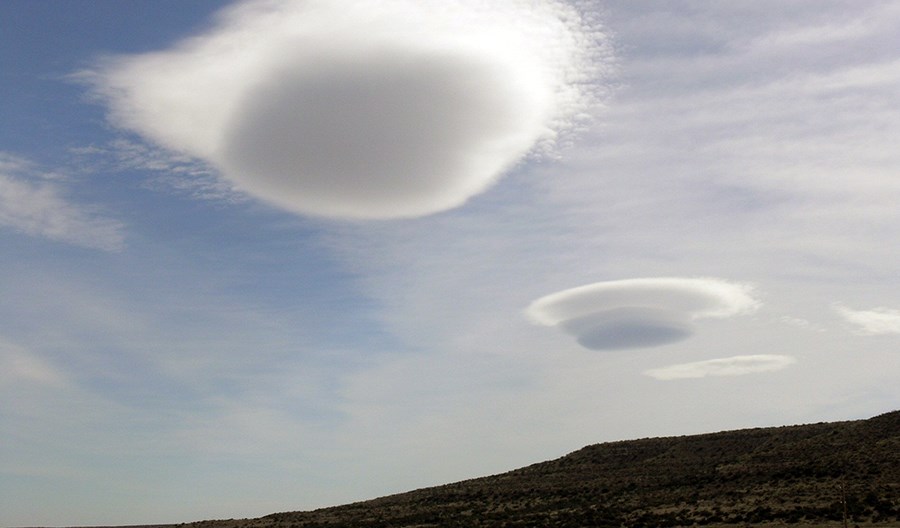 Two saucer shaped clouds over a desert hill.