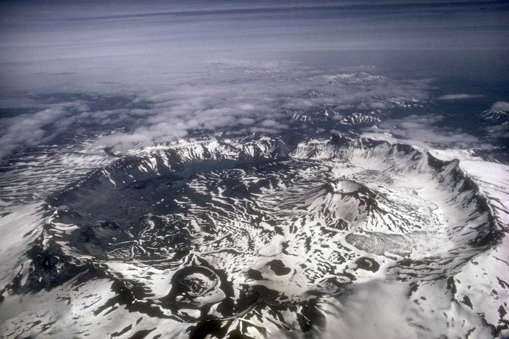 aerial photo of a summit caldera, with a deep crater and snow and clouds