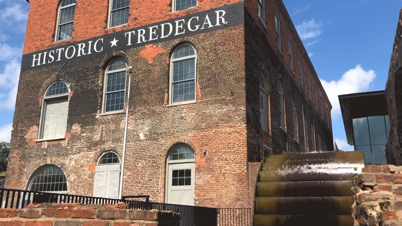 Tredegar water wheel GIF Water wheel spinning, with water splashing and glistening over it in the sun, next to a three-story brick building with the text "HISTORIC TREGEDAR" painted on the front of it just above the second story windows.