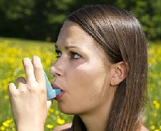 A woman outdoors using her inhaler.