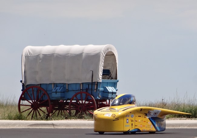 Solar car next to a covered wagon.