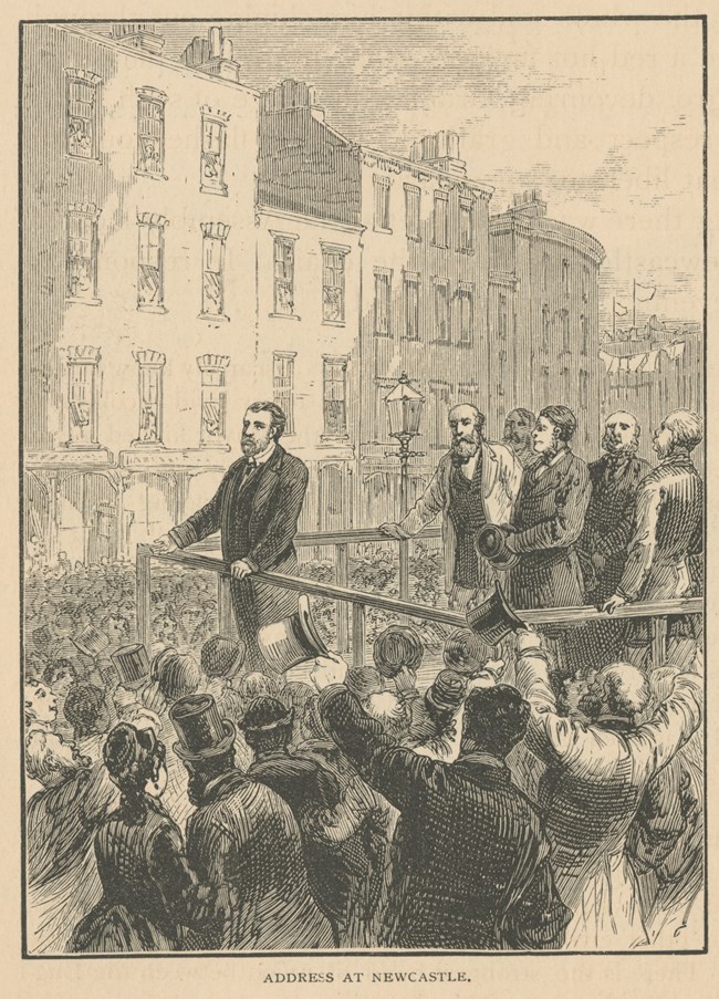 Bearded man in suit addressing thousands of people in a busy urban center. Text reads "Address at Newcastle."