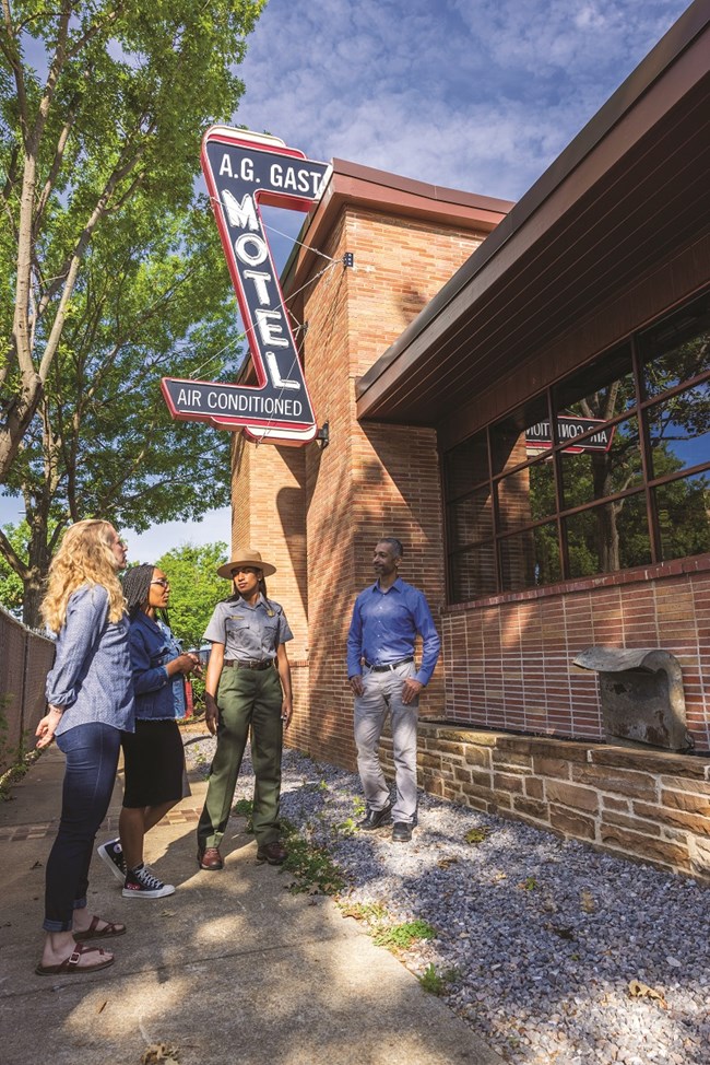 three people and a park ranger talking outside the AG Gaston Motel made out of red bricks