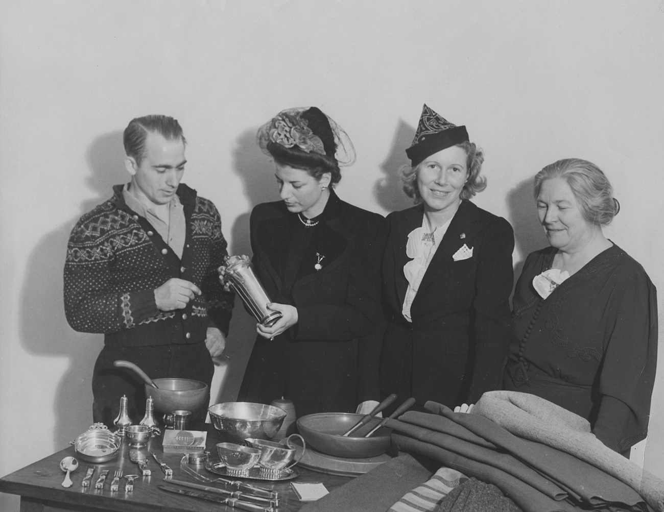 lt= A man and three women stand behind a table displaying petwer and woolen cloth.